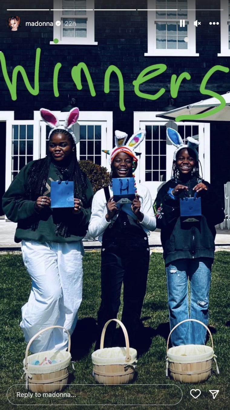 Three young Black women smile in front of a house holding blue gift bags while wearing easter bunny ears/