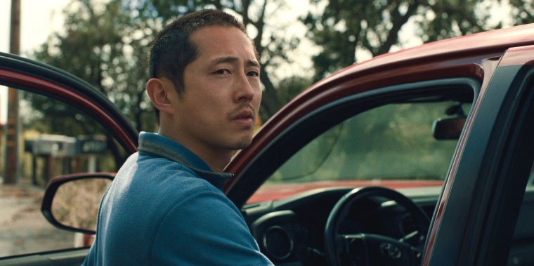 Yeun looks over his shoulder next to his red toyota tacoma pickup truck.