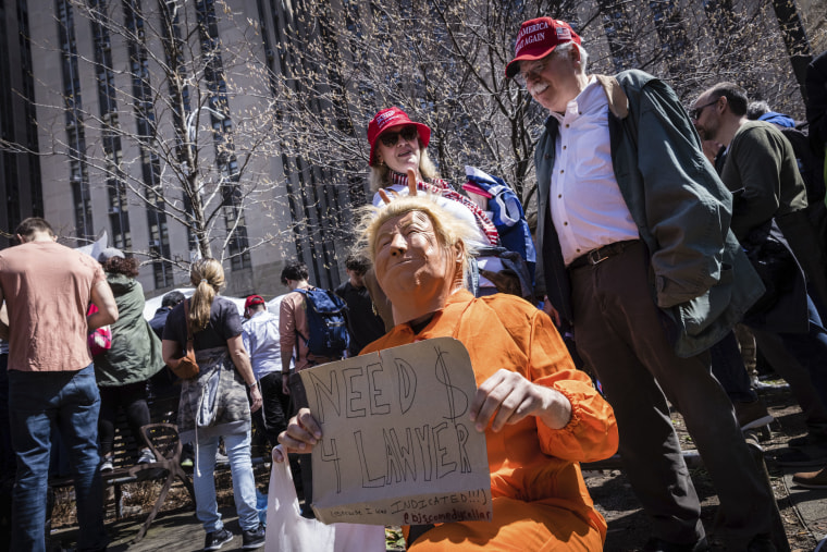 A person dressed as former President Donald Trump in an orange prison jumpsuit poses in front of Trump supporters.