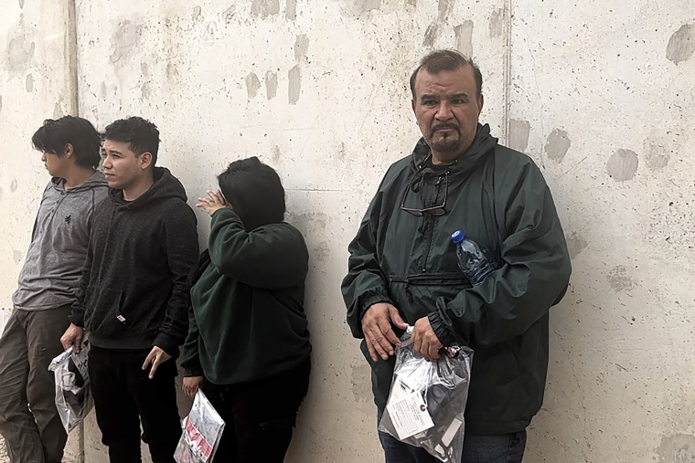 A man from Mexico along with a Mexican woman and two men from El Salvador stand by the border wall after being apprehended by Border Patrol on May 4, 2023. 