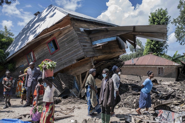 People walk next to a house destroyed by the floods in Nyamukubi, Congo