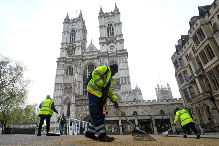 Workers use rakes to cover the road with sand outside of Westminster Abbey in London
