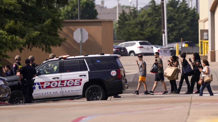 People raise their hands as they leave a shopping center after a shooting on May 6, 2023, in Allen, Texas.