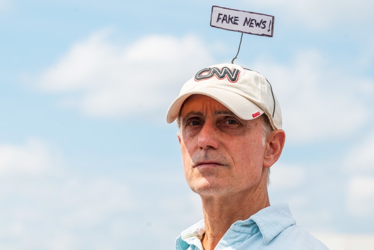 A man wears a Fake News sign on top of a CNN hat while waiting in line for a Trump rally in Wilkes-Barre-Barre Township, Pa., in 2022.