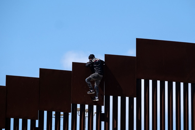 A migrant climbs over the border fence into the United States after fetching groceries for other migrants waiting to be processed by authorities on the U.S. side of  border on May 10, 2023.