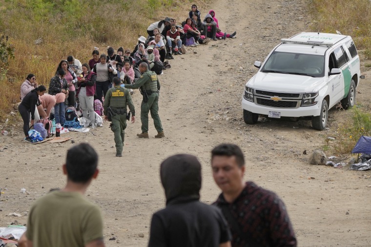 U.S. Border Patrol agents talk with women before leading them to a van as they wait to apply for asylum between two border walls on May 11, 2023, in San Diego. 