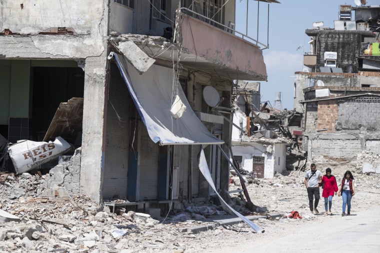 Residents walk past the damaged remains of a building in Antakya, Turkey