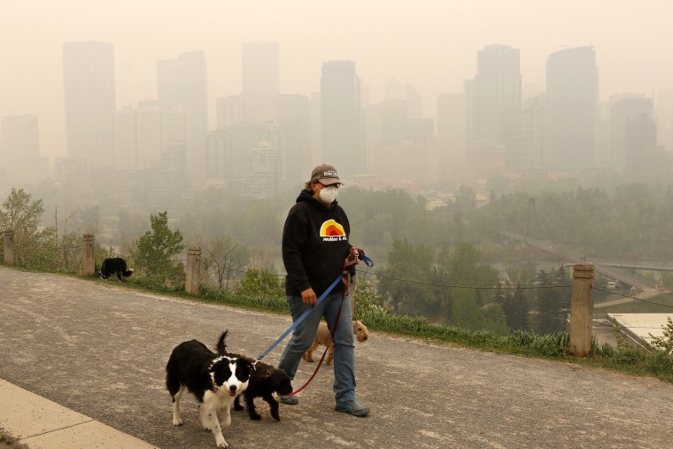 Wearing a protective mask, dog walker Leslie Kramer ventures out as heavy smoke from northern Alberta forest fires comes south to blanket the downtown area in Calgary, Canada, Tuesday, May 16, 2023. (Larry MacDougal/The Canadian Press via AP)