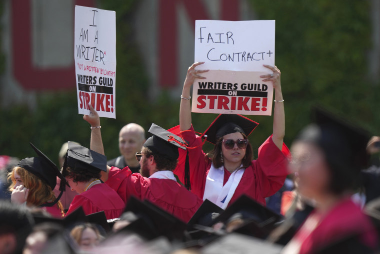 Graduating students hold signs in support of the Hollywood writers' strike during David Zaslav's commencement speech