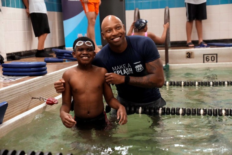 Cullen Jones standing next to a child in the pool during a swimming lesson.