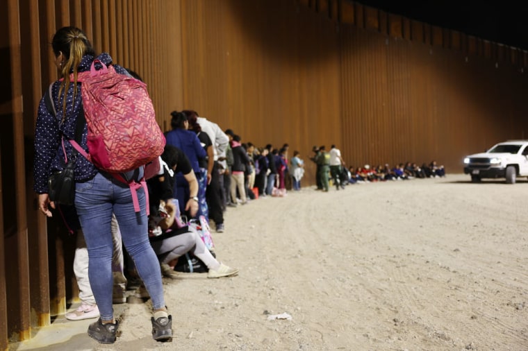 Un grupo de migrantes espera junto al muro fronterizo las instrucciones de las autoridades estadounidenses para ser procesados tras el fin del Título 42 en Yuma, Arizona, el 11 de mayo de 2023.