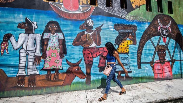Una mujer viendo su teléfono celular camina al lado de un mural celebrando las herencias negras afuera del Museo de las Culturas Afromestizas en Guerrero, México, en 2020 