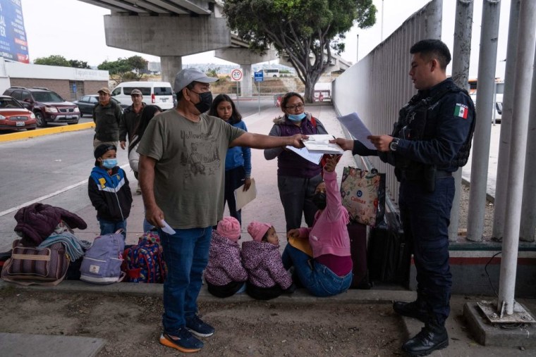 Un policía mexicano pide los documentos a una familia de migrantes que arribó para una cita con las autoridades estadounidenses en el puerto de entrada de El Chaparral, en Tijuana, México, el 12 de mayo de 2023.
