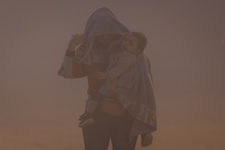 Una madre inmigrante de Venezuela y su hijo caminan a través de una tormenta de polvo en un campamento improvisado entre el Río Grande y la valla fronteriza entre Estados Unidos y México mientras esperan ser procesados para solicitar asilo el 10 de mayo de 2023 en El Paso, Texas.
