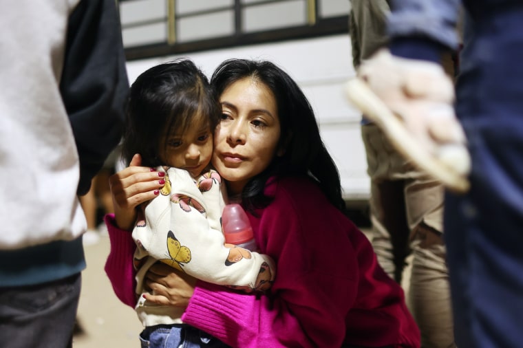 Inmigrantes peruanos que buscan asilo en los Estados Unidos se abrazan mientras esperan para abordar un autobús durante el procesamiento por parte de agentes de la Patrulla Fronteriza en las primeras horas de la mañana tras cruzar a Arizona desde México el 11 de mayo de 2023 en Yuma, Arizona.