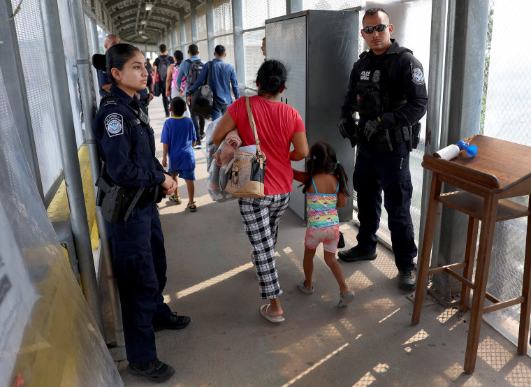 Miembros del departamento de Aduanas y Protección Fronteriza observan cómo los migrantes cruzan el Puente Internacional Matamoros-Brownsville hacia los Estados Unidos después de obtener una cita para ingresar legalmente al país el 12 de mayo de 2023 en Brownsville, Texas.