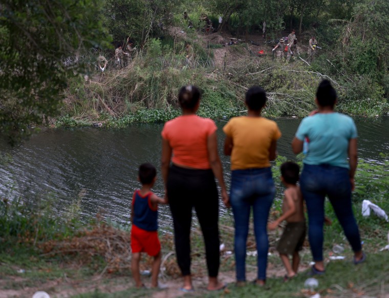 Migrantes observan cómo miembros de la Guardia Nacional de Texas despejan un área del lado estadounidense del Río Grande el 12 de mayo de 2023 en Matamoros, México.