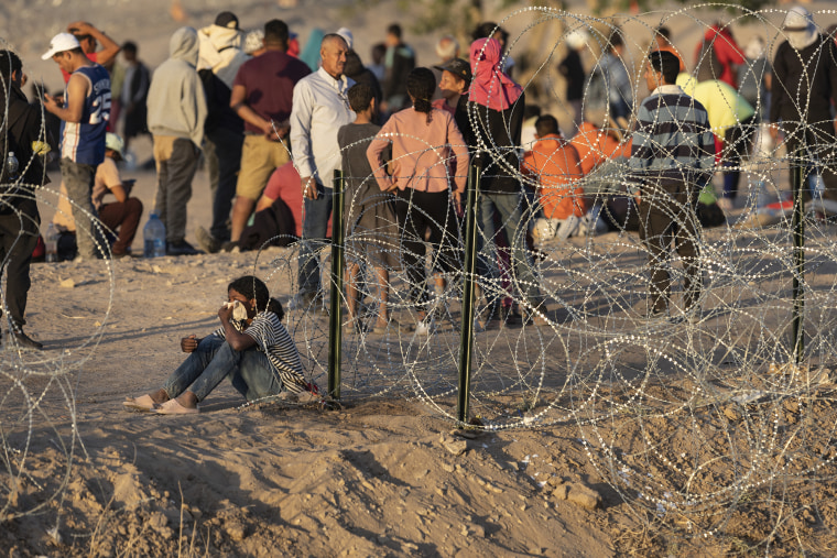 Inmigrantes esperan cerca de la valla fronteriza entre Estados Unidos y México después de cruzar a El Paso, en Texas.