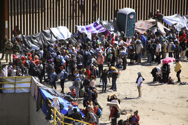 Cientos de migrantes esperan junto al muro fronterizo a ser procesados por agentes de Estados Unidos entre San Diego y Tijuana, México.