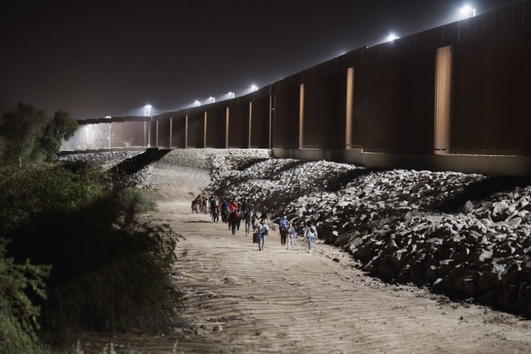 Migrantes caminan a lo largo del muro fronterizo antes de entregarse a los agentes de la Patrulla Fronteriza de EE.UU. después de cruzar la frontera con México horas antes del levantamiento del Título 42 en Yuma, Arizona, el 10 de mayo de 2023.