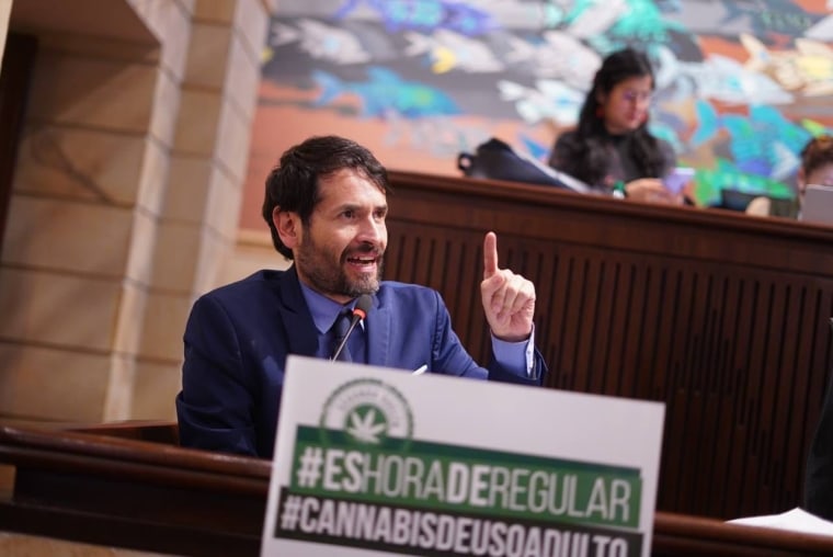 El congresista de colombia Juan Carlos Losada habla frente a un micrófono en la Cámara de Representantes, detrás de un cartel que dice "Es hora de regular: cannabis de uso adulto"