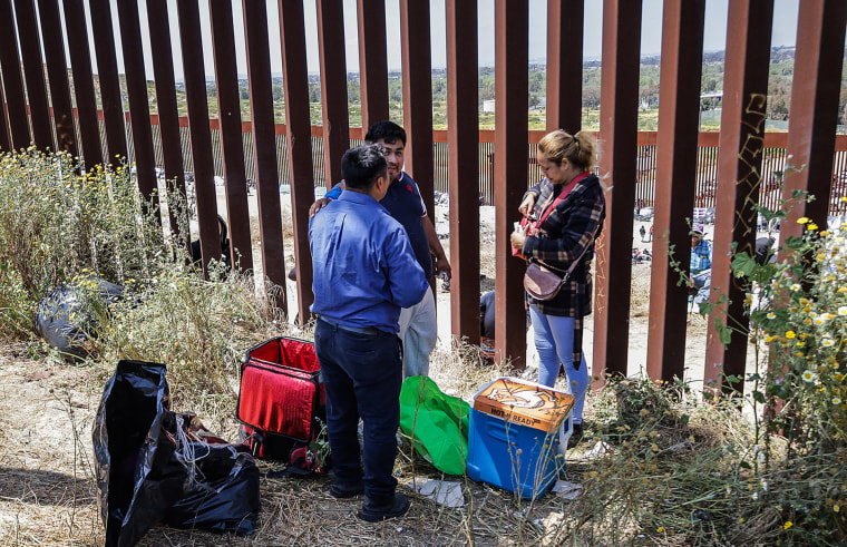 Repartidores de comida rápida entregan pedidos a migrantes en el muro fronterizo en Tijuana, Baja California, el 11 de mayo de 2023.