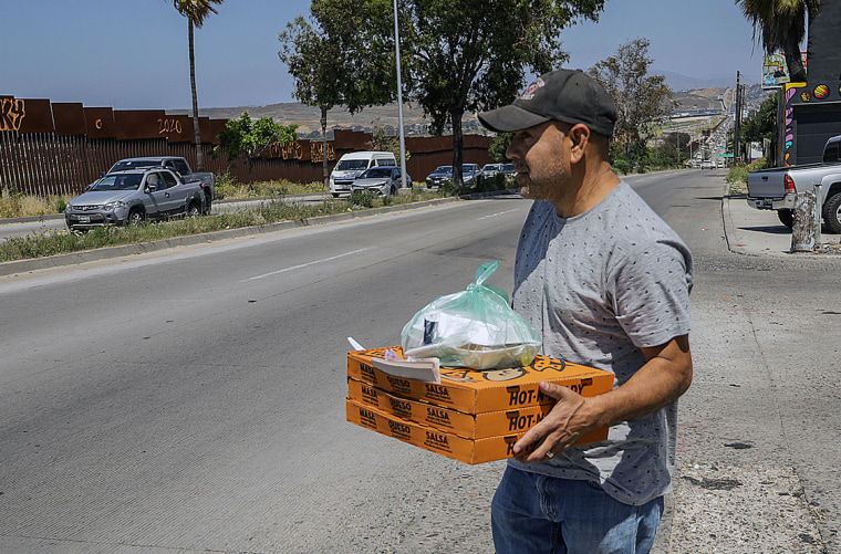 Los repartidores de comida rápida en  Tijuana comenzaron a llegar este jueves a los linderos del campamento entre los muros fronterizos.