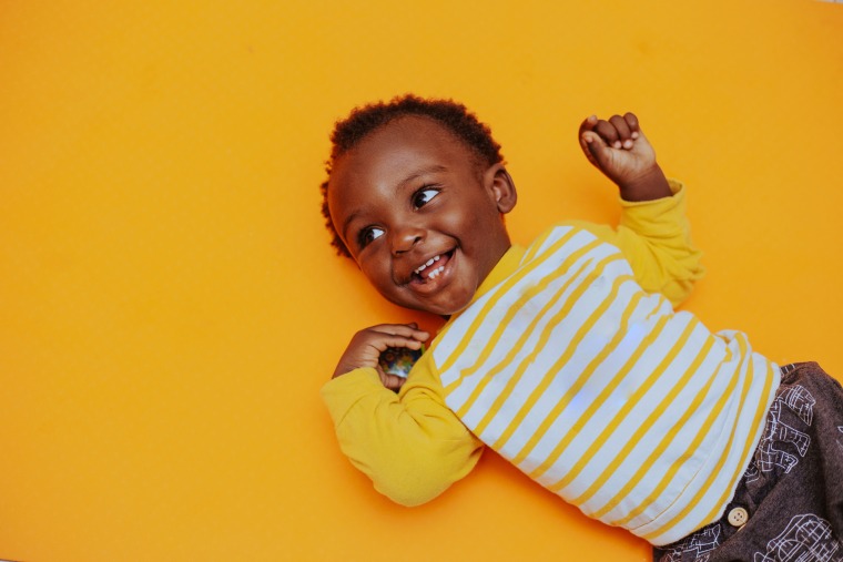 Portrait Of Smiling Black Boy Lying On Yellow Background, Tema, Ghana