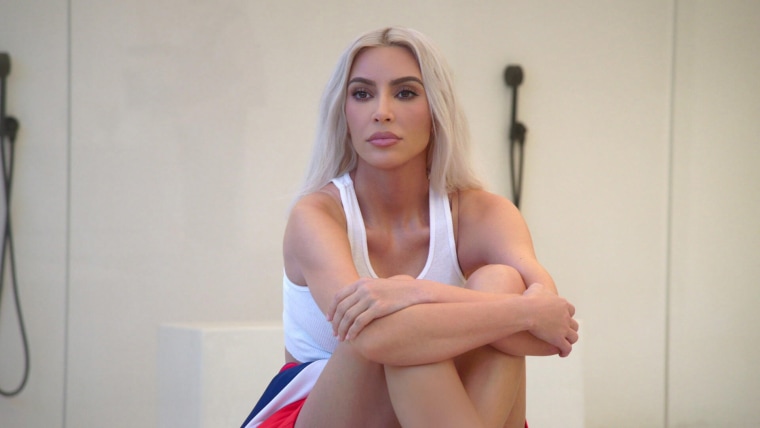 Kim Kardashian sits on a countertop in a white tank top.