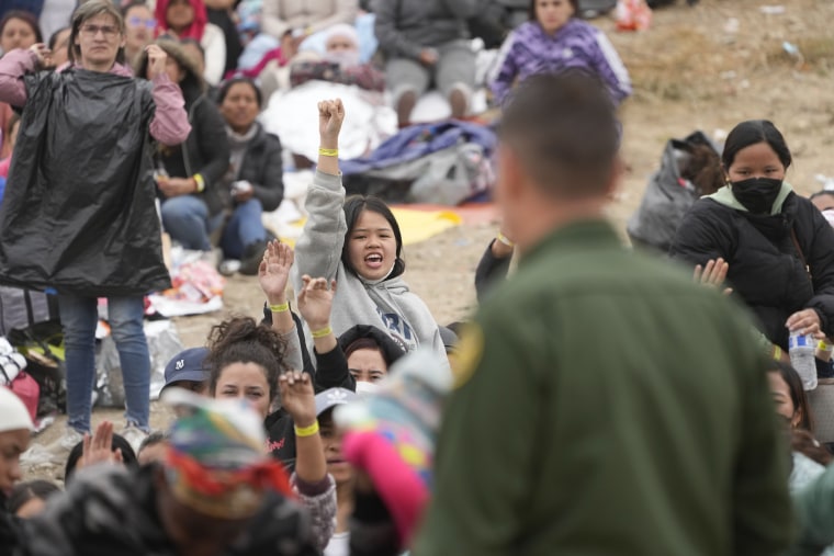 Varias mujeres migrantes alzan su mano con pulseras este viernes 12 de mayo, esperando ser escogidas por agentes fronterizos para aplicar por asilo después de esperar varios días en un punto fronterizo de San Diego, California. 