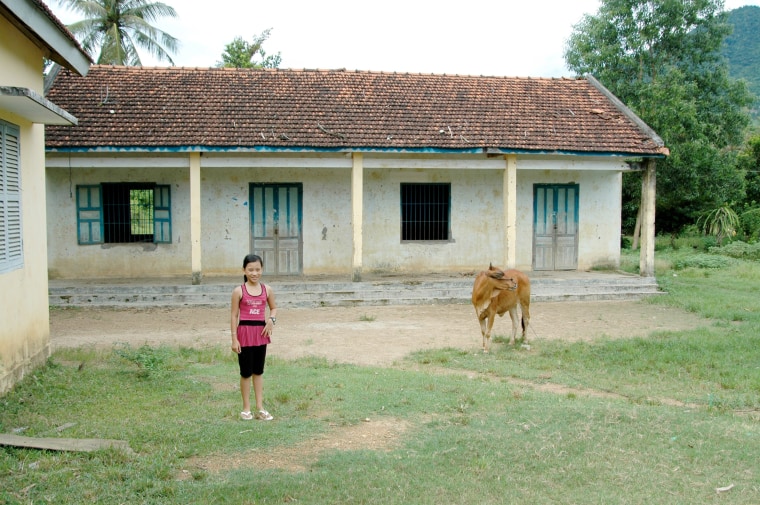 Ha Nguyen in 2008 outside her old schoolhouse in Vietnam. The students drank a glass of milk every day supplied by the cow tied up outside.