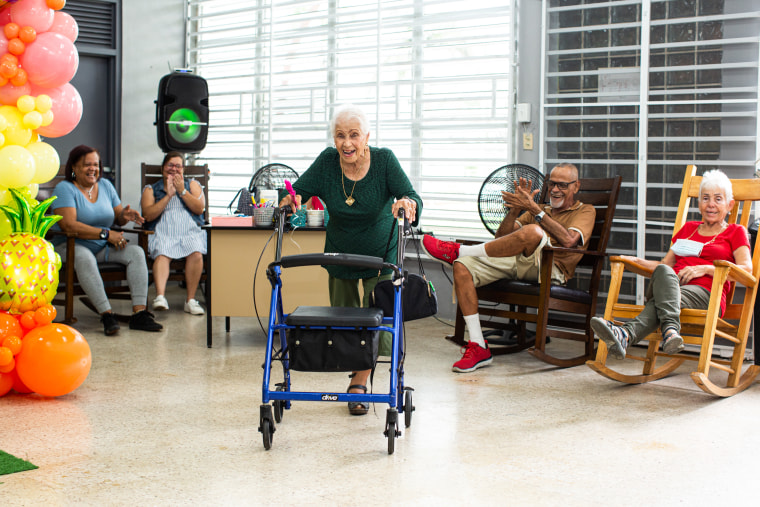 Julia Canals Solis, 96, dances a bolero with her walker as others cheer her on at the Center for Activities and Multiple Uses for the Elderly of Toa Baja in Toa Baja, Puerto Rico, on May 26, 2023.