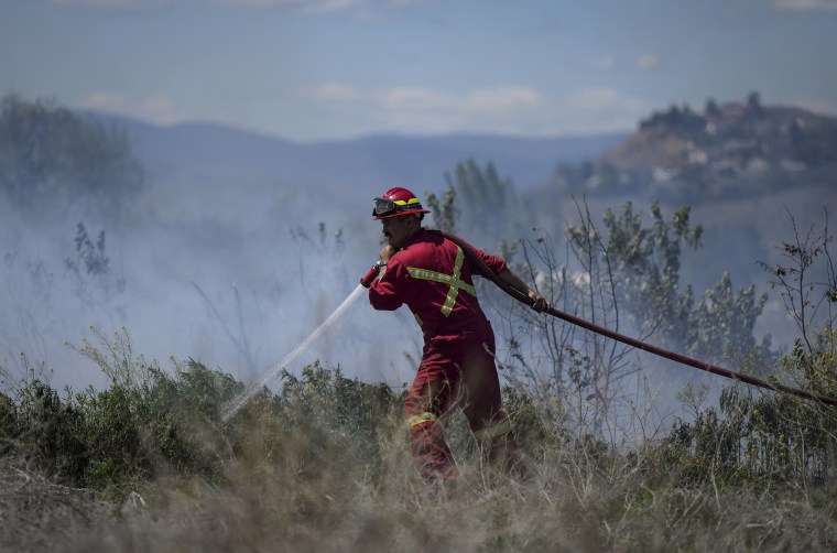 A firefighter directs water on a grass fire on an acreage behind a residential property in Kamloops, British Columbia, on June 5, 2023.