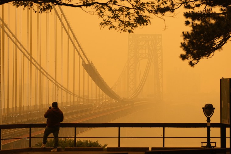 A man talks on his phone as he looks through the haze at the George Washington Bridge from Englewood Cliffs, N.J