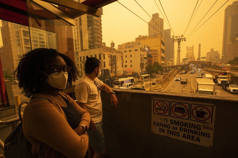 People wear masks as they wait for the tramway to Roosevelt Island as smoke from Canadian wildfires casts a haze over New York City on June 7, 2023.