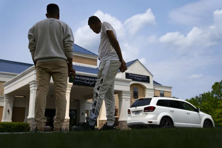 Mohamed, a 19-year-old fleeing political persecution in the northwest African country of Mauritania, center, watches as car services arrive to shuttle outbound migrants away from the Crossroads Hotel, in Newburgh, N.Y