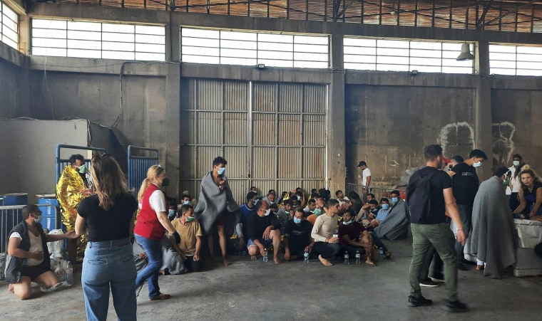 Survivors of a shipwreck sit in a warehouse, at the Greek port town of Kalamata on Wednesday.