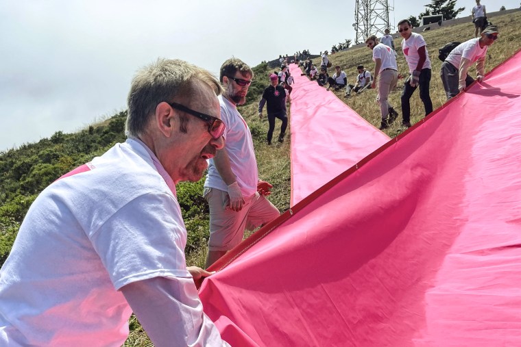 Image: Patrick Carney, left, Co-Founder of Friends of the Pink Triangle, works with volunteers laying out pink tarps to form the shape of a pink triangle on Twin Peaks in San Francisco on June 16, 2023. 
