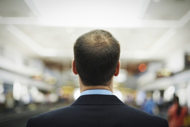 Mid adult balding business man standing at airport, rear view