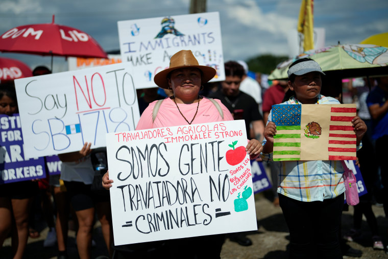 A woman carries a sign that reads: "We are working people, not criminals; we are the ones who harvest the crops; Immokalee farm workers strong" as hundreds gathered on June 1 in Immokalee, Fla. to protest Florida Senate bill 1718, which imposes restrictions on undocumented immigrants.