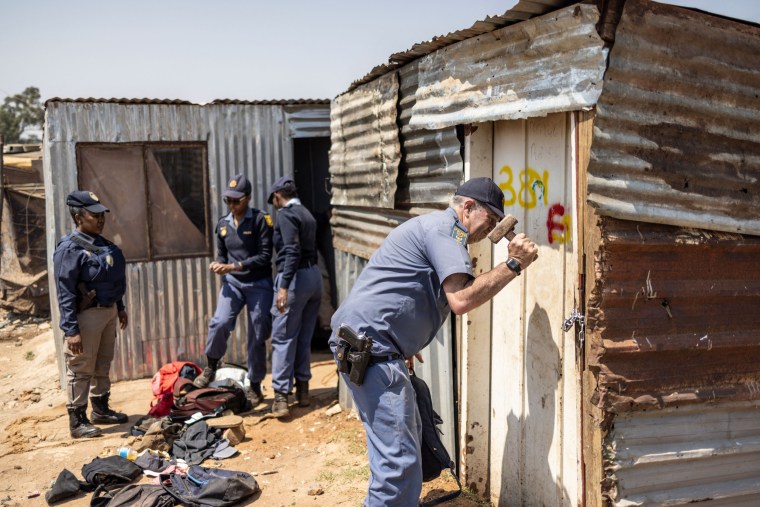 A police officer uses a hammer to break into the shack of a suspected illegal miner in Florida, near Johannesburg, South Africa, on Sept. 28, 2022 during a police raid aimed at arresting immigrants involved in illicit gold mining operations. 