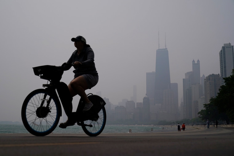 A person rides a bicycle along the shore of Lake Michigan as the downtown skyline is blanketed in haze from Canadian wildfires Tuesday, June 27, 2023, in Chicago. 