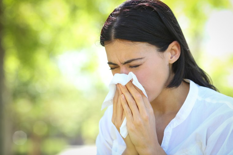 Ill woman sneezing covering mouth with a wipe in a park