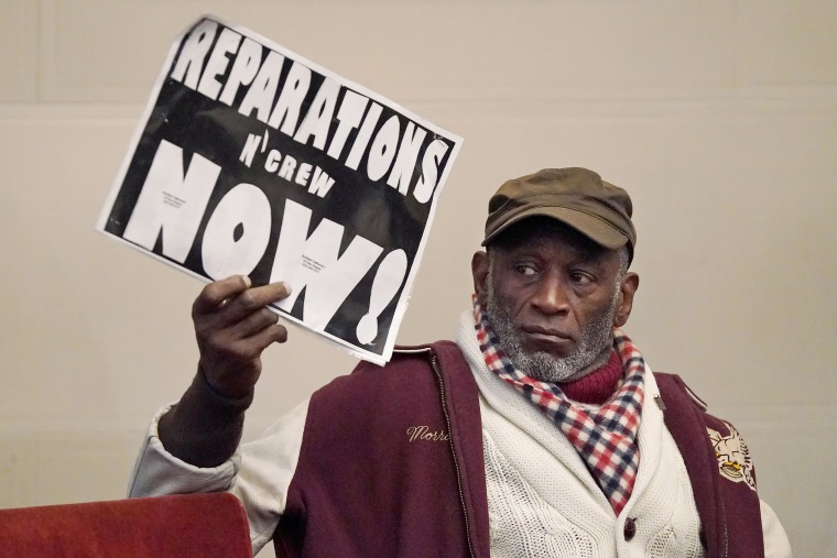 Morris Griffin holds up a sign during a meeting of California's reparations task force in Oakland on Dec. 14, 2022.