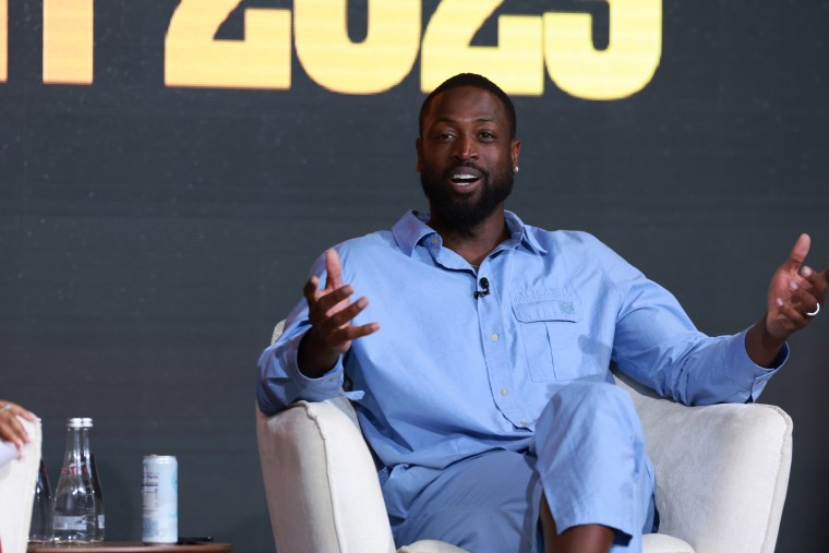 Wade in an all-blue outfit smiles and talks onstage.