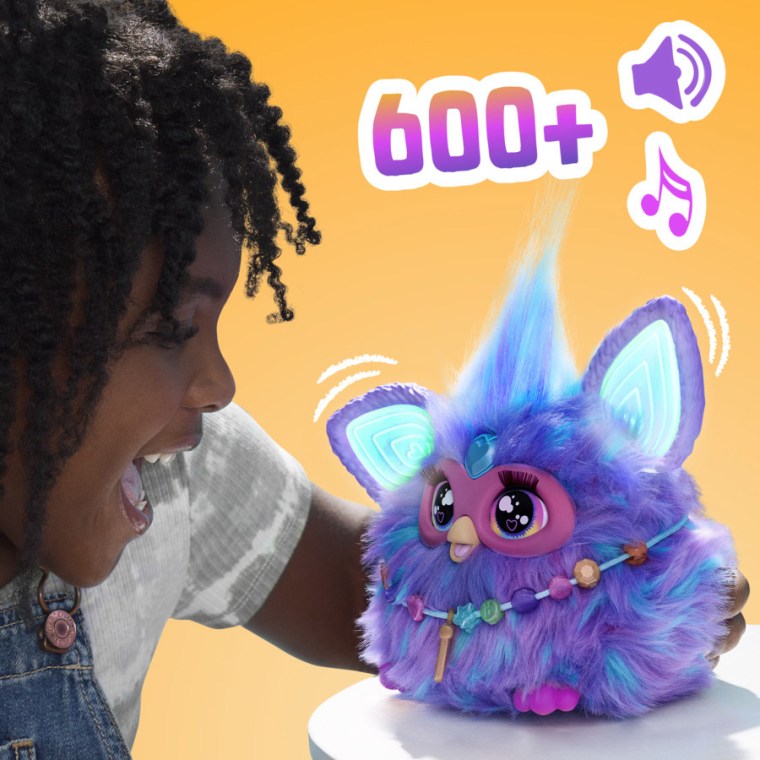 Un enfant sourit à côté d'un furby bleu et violet qui semble parler.