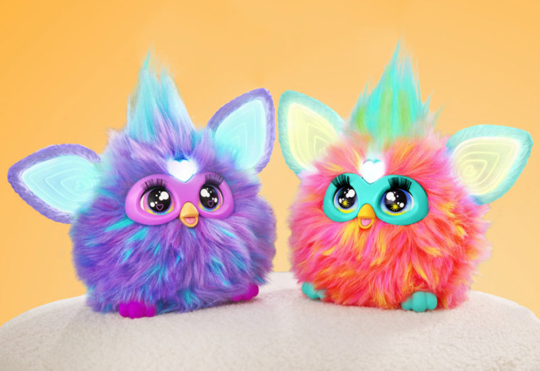 Deux furbies, un violet et un rose, avec des cheveux mohawk bleus devant un fond orange.