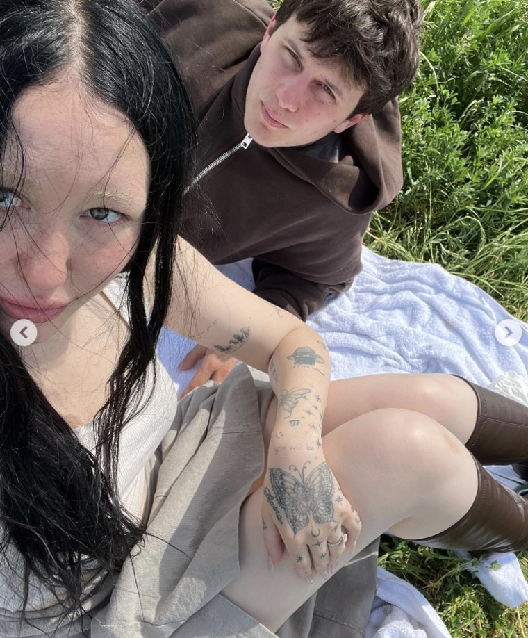 Noah Cyrus and Pinkus sit on a blanket on green grass and take a selfie.