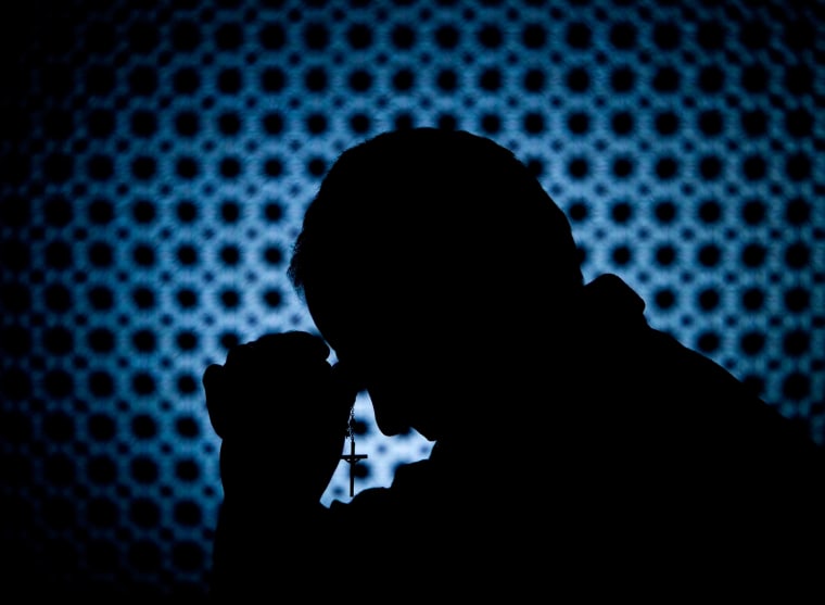 Priest in confession booth with cross