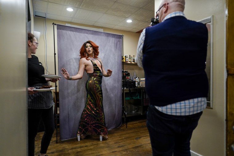 A waitress pauses with plates of food as drag queen Harpy Daniels poses for a photograph before the "Daniels Family Values" drag show at the Heritage Restaurant in Shamokin, Pa., on April 16, 2022.